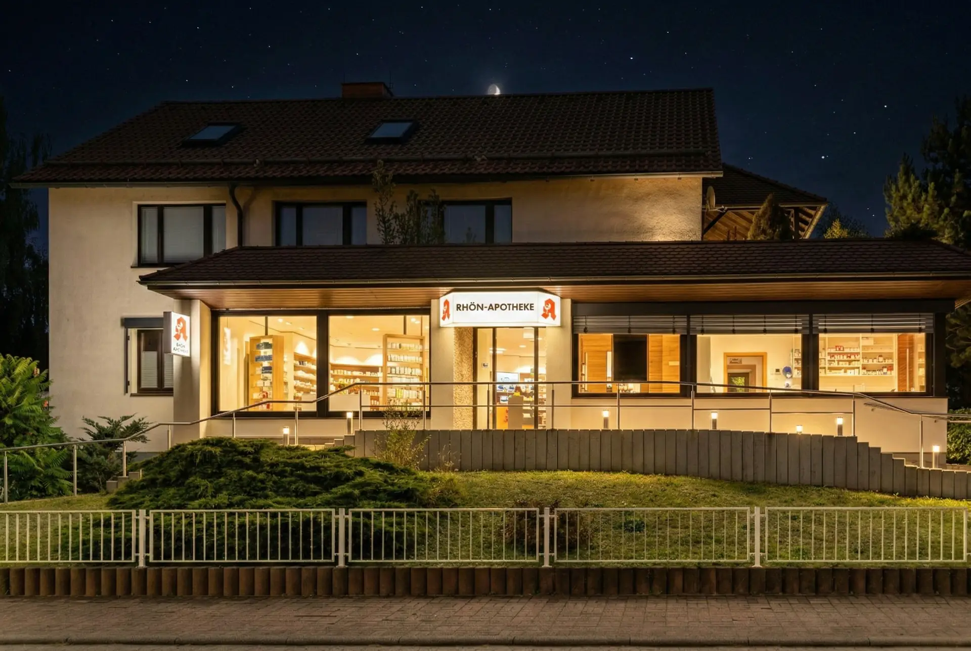 Im nächtlichen Außenbereich leuchtet das Schild der Rhön Apotheke Kaltennordheim, warmes Licht am Eingang, mit Fokus auf den Apotheken-Notdienst.